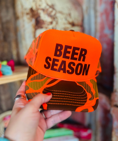 Trucker baseball cap black and orange. polyester front with "Beer Season" printed in black lettering. The bill is orange; black and green camo the back is mesh and adjustable