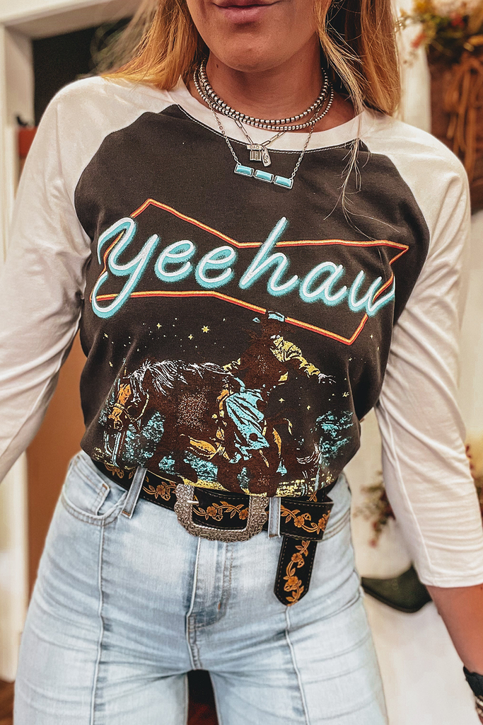 Western style raglan graphic T with white sleeves and dark brown trunk with blue/turquoise "yeehaw" lettering. The graphic is silhouetted of a rider on a horse.