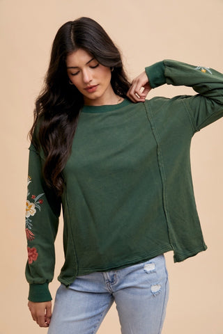 This hunter green sweatshirt like top has floral embroidered sleeves and a comfortable neckline